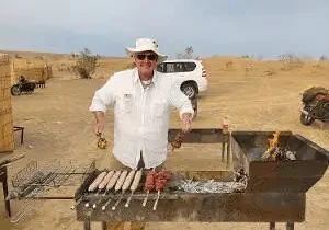 Man grilling sausages outdoors in desert.